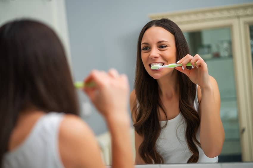 Young woman brushing teeth in front of her bathroom mirror