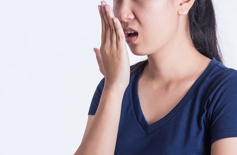 Young woman with porcelain veneers breathing into her hand. Some recent dental work may be causing her bad breath