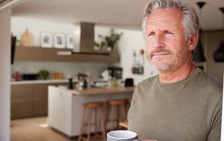 Middle aged man standing in his kitchen looking out the door with his cup of coffee. When we have a headache we often go for a cup of caffeine. Is that coffee actually causing your headaches?