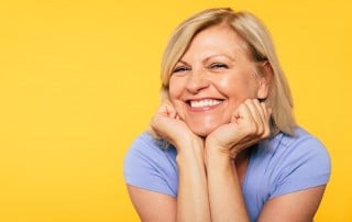 Mature woman stands in front of a yellow background, showing her amazing non-surgical facelift off