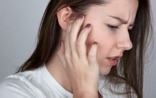 woman with an itchy ear, suffering from TMJ